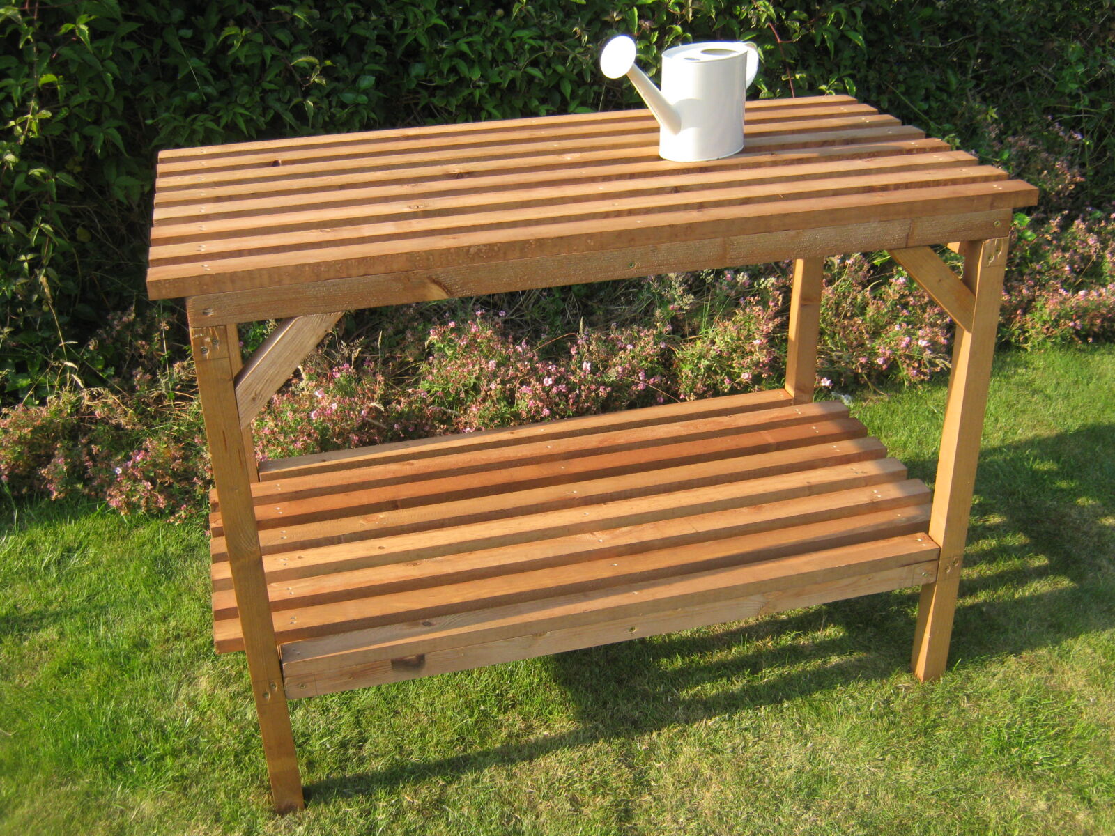Two-tier wooden greenhouse staging with a watering can and plant pot on top - Greenhouse Staging