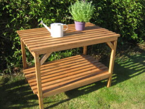 Two-tier wooden greenhouse staging with a watering can and plant pot on top, set on a lawn - Greenhouse Staging