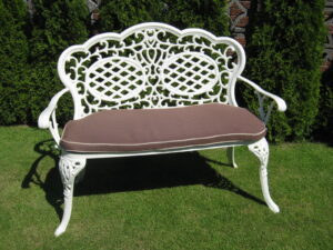 White ornate metal garden bench with a brown cushion on a lawn - Greenhouse Staging